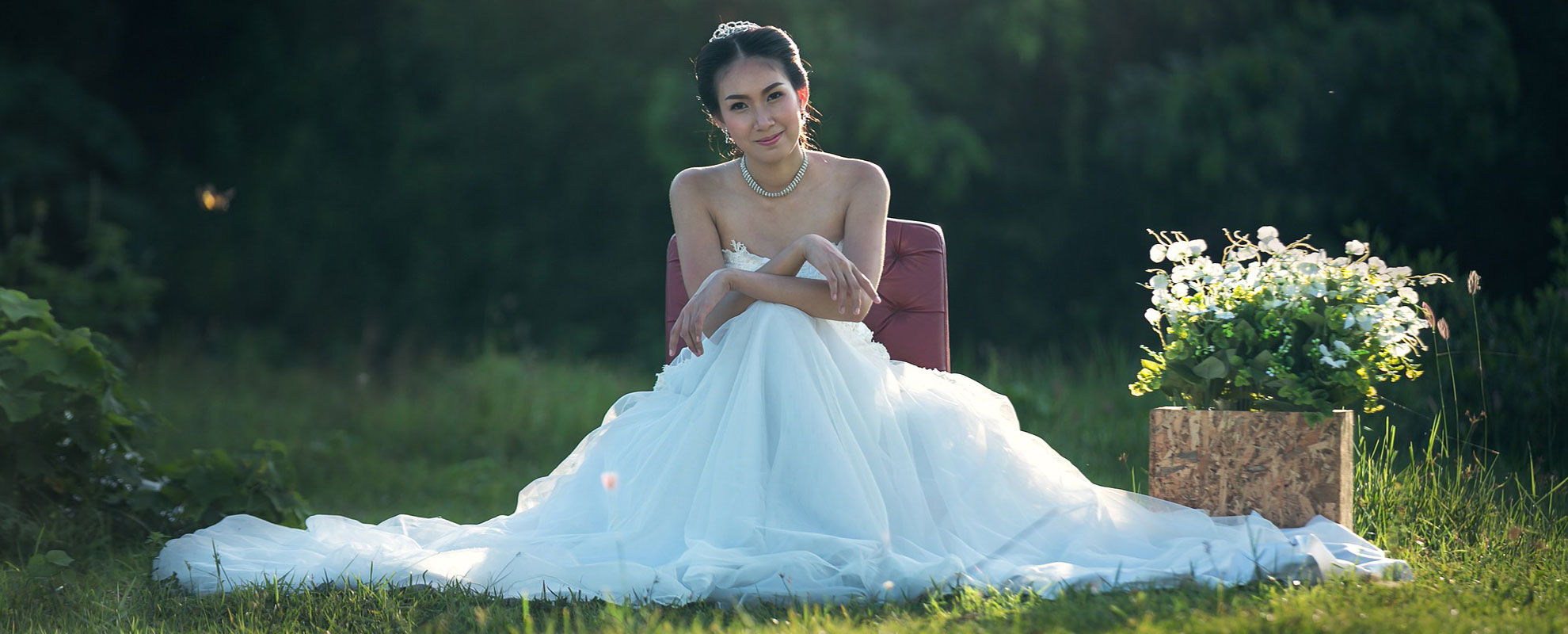 a young bride in a wedding dress sitting outside in a green field
